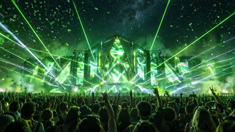 Nocny koncert na festiwalu muzyki elektronicznej: tłum z uniesionymi rękami, zielone lasery nad sceną